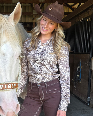 Woman wearing a brown and cream lace shirt standing next to a horse.