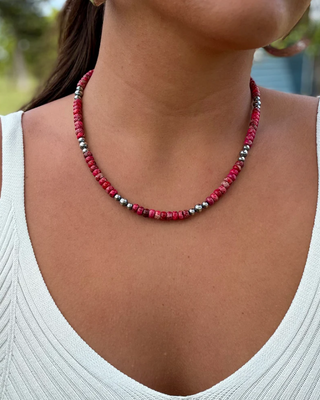 Person wearing a red and silver beaded necklace with a blurred outdoor background