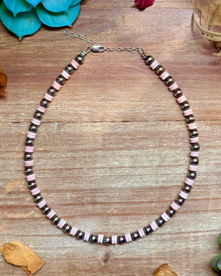 Necklace with pink and black beads on a wooden surface with decorative elements