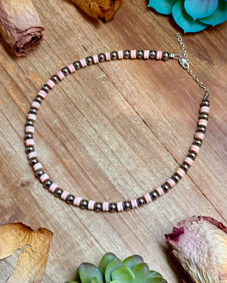 Necklace with pink and silver beads on a wooden surface with dried flowers and succulents.