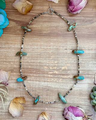 Necklace with turquoise beads on a wooden surface with flowers and plants