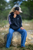Woman sitting on a rock outdoors wearing a black sweatshirt and blue jeans.