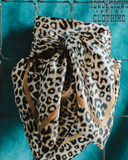 The Liberty Leopard Wild Rag tied onto a metal rack in a turquoise background. 