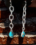 Silver chain earrings with faux turquoise stones on a stone surface