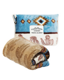 The Cactus Stripe Travel Blanket rolled up with the blankets bag behind it in a white backdrop.