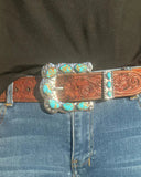 Person wearing blue jeans with a decorative belt featuring a large buckle.