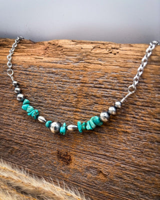 A silver chain necklace with turquoise and silver beads, displayed on a rustic piece of wood.