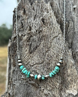 Necklace with turquoise and silver beads hanging on a wooden post.