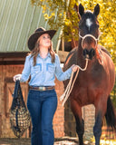 Woman in cowboy hat with a horse in front of a wooden building