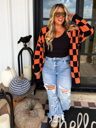 Woman wearing an orange and black checkered cardigan in front of a door with Halloween decorations.