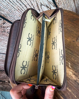 An open brown leather zippered wallet or travel organizer held in a hand, showing a tan interior printed with the Countryside Co. logo.