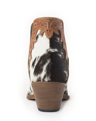 A single western ankle boot shown from the back, featuring a black and white cowhide body with tan tooled leather trim and a brown stacked heel, set against a plain white background.