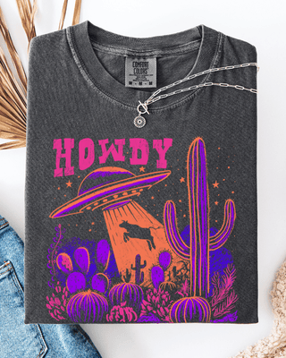Dark gray t-shirt with 'HOWDY' design featuring a UFO and cacti, displayed with jeans and a hat.