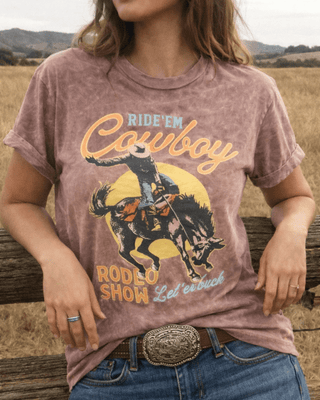 Person wearing a graphic t-shirt with a cowboy design and text, standing outdoors.