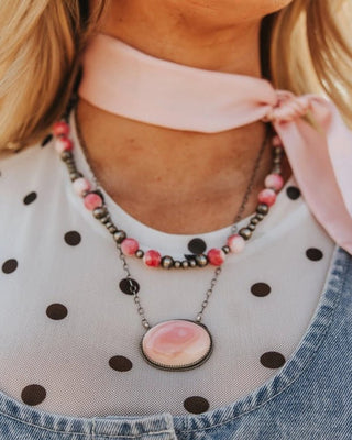 Person wearing a polka dot shirt and denim overalls with a pink ribbon, outdoors.