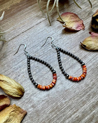 Teardrop-shaped beaded earrings on a wooden surface with dried leaves and plants.