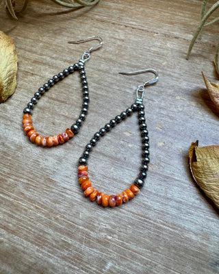 Pair of beaded earrings on a wooden surface with natural elements.