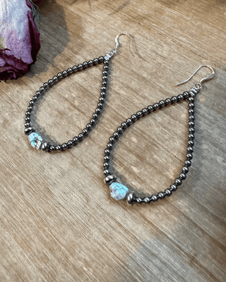 Teardrop-shaped beaded earrings on a wooden surface with a dried rose.