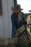 Person in cowboy hat and blue shirt handling hay near a white building
