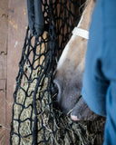Person in blue jacket interacting with a horse eating from a hay net.