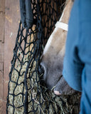 Person in blue jacket interacting with a horse eating from a hay net