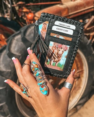 Hand holding a black leather wallet with card slots against a rustic background