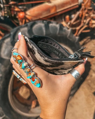 Hand holding a small black pouch with a rustic background featuring old vehicles.
