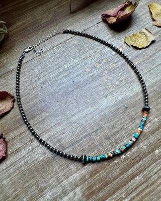 Necklace with black beads and colorful accents on a wooden surface with dried leaves.