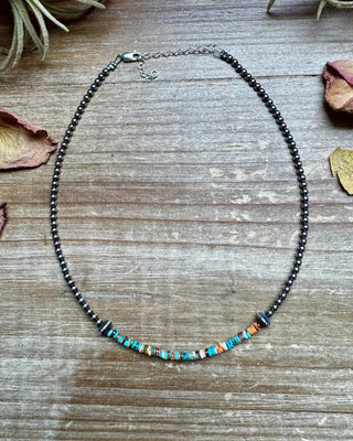 Necklace with colorful beads on a wooden surface with dried leaves and plants.