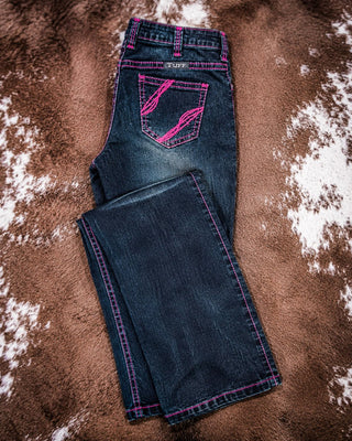A pair of dark blue denim jeans with bright pink contrast stitching and a matching pink embroidered back pocket design, laid flat on a brown and white cowhide rug.