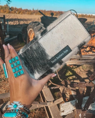 Hand holding a leather wallet with turquoise jewelry in front of a rustic background with a tractor.