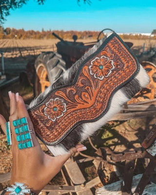 Decorative wallet with intricate patterns held by a hand wearing turquoise jewelry in an outdoor setting.