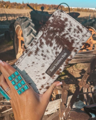 Hand holding a cowhide wallet with a blurred background of a tractor and field.
