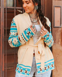 Woman wearing a cream-colored cardigan with blue and white patterns, standing in front of a wooden door.