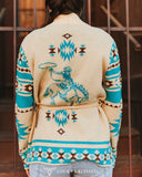 Person wearing a patterned sweater with a design of a person on a horse, standing in front of a wooden wall.