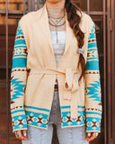 Person wearing a cream-colored cardigan with blue and brown pattern, standing against a wooden background.