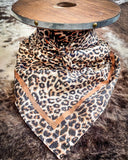 The Liberty Leopard Wild Rag tied around a wooden cable reel, resting on a backdrop of cowhide.