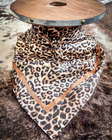 The Liberty Leopard Wild Rag tied around a wooden cable reel, resting on a backdrop of cowhide.