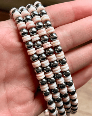 Three beaded necklaces with pink and silver beads laying over a hand.