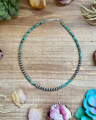 Necklace with turquoise and black beads on a wooden surface with flowers and plants.
