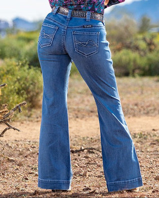 Person wearing a floral shirt, blue jeans, and a black cowboy hat in a desert landscape.