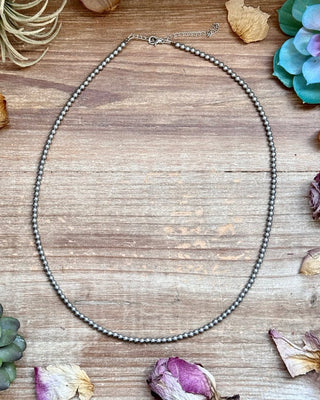Silver necklace on a wooden surface with succulents and dried flowers