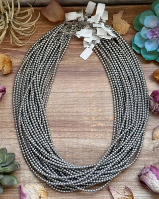 Necklace with multiple strands on a wooden surface with succulents and dried flowers.