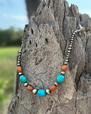 Necklace with turquoise and orange beads on a wooden post outdoors