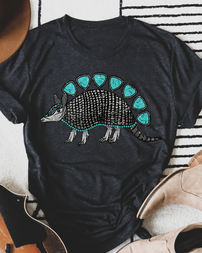 Black t-shirt with armadillo graphic on a striped surface with boots and a hat.
