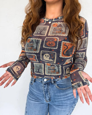 Person wearing a Halloween-themed long-sleeve shirt with pumpkins, ghosts, and cats on a white background.