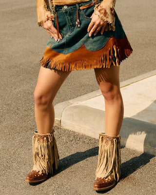 Person wearing a distressed top, denim skirt, and fringed boots in an outdoor setting.