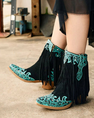Black boots with turquoise embroidery and fringe in a rustic setting