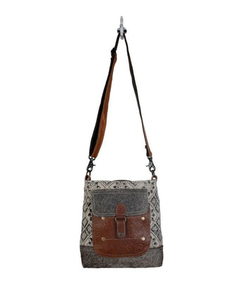 Crossbody bag with brown leather flap and patterned fabric on a white background