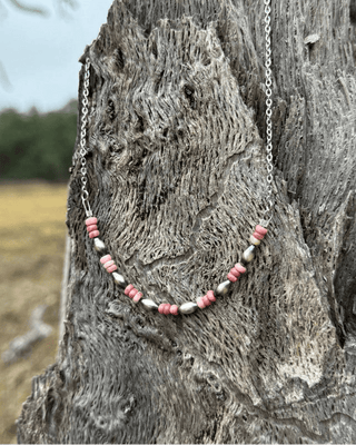 Necklace with pink and silver beads on a textured wooden surface